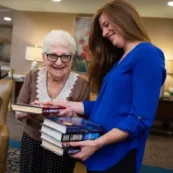 An Artman team member and a resident look at a stack of fiction books